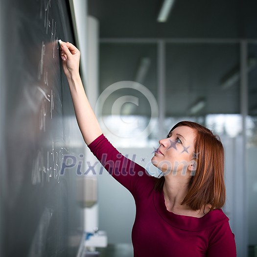 Pretty, young college student writing on the chalkboard, blackboard during a math class Pretty, young college student writing on the chalkboard, blackboard during a math class