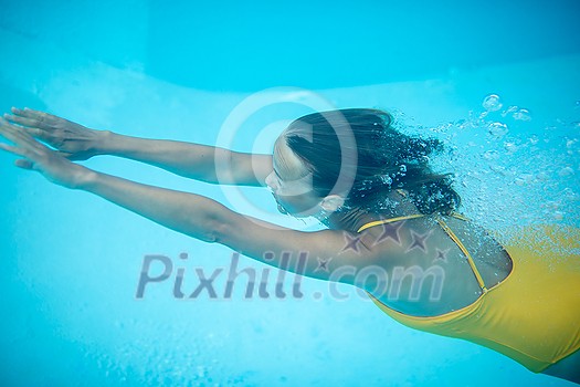 Gorgeous young woman in a pool, jumping and diving underwater, having fun