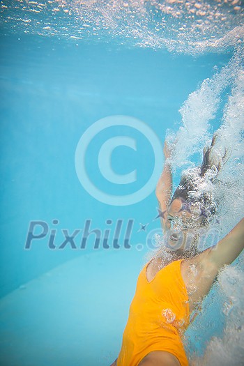 Gorgeous young woman in a pool, jumping and diving underwater, having fun