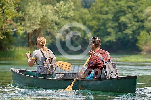 Couple adventurous explorer friends are canoeing in a wild river surrounded by the beautiful nature Couple adventurous explorer friends are canoeing in a wild river surrounded by the beautiful nature