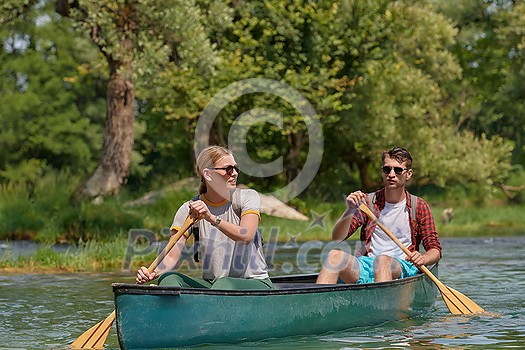 Couple adventurous explorer friends are canoeing in a wild river surrounded by the beautiful nature Couple adventurous explorer friends are canoeing in a wild river surrounded by the beautiful nature