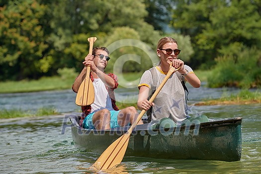 Couple adventurous explorer friends are canoeing in a wild river surrounded by the beautiful nature Couple adventurous explorer friends are canoeing in a wild river surrounded by the beautiful nature