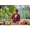 Man cooking tasty food on barbecue grill for outdoor french dinner party near the river on beautiful summer evening in nature