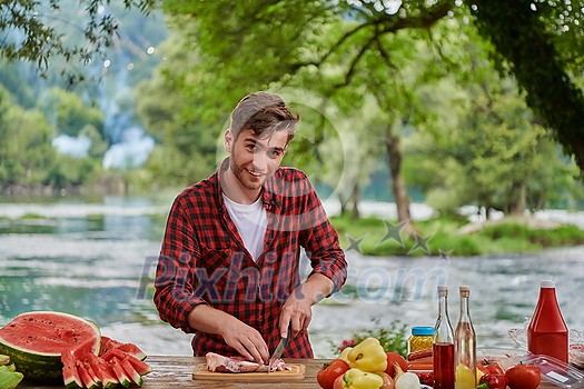 Man cooking tasty food on barbecue grill for outdoor french dinner party near the river on beautiful summer evening in nature Man cooking tasty food on barbecue grill for outdoor french dinner party near the river on beautiful summer evening in nature