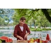 Man cooking tasty food on barbecue grill for outdoor french dinner party near the river on beautiful summer evening in nature