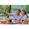 young happy couple taking selfie while having picnic french dinner party outdoor during summer holiday vacation near the river at beautiful nature