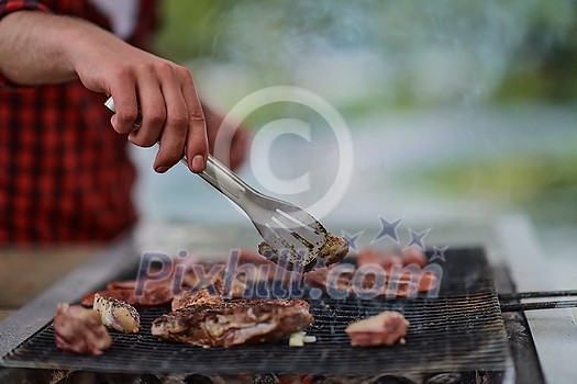 Man cooking tasty food on barbecue grill for outdoor french dinner party near the river on beautiful summer evening in nature