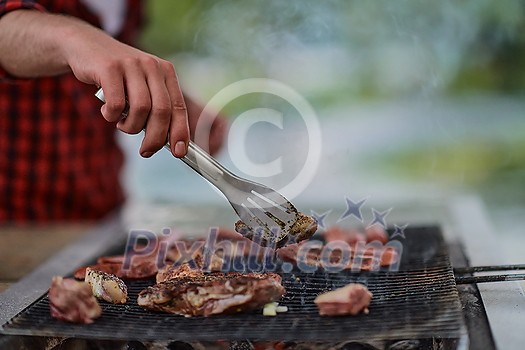 Man cooking tasty food on barbecue grill for outdoor french dinner party near the river on beautiful summer evening in nature Man cooking tasty food on barbecue grill for outdoor french dinner party near the river on beautiful summer evening in nature