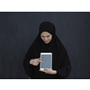 Young Arab businesswoman in traditional clothes or abaya and glasses showing tablet computer display in front of black chalkboard representing modern islam fashion and technology