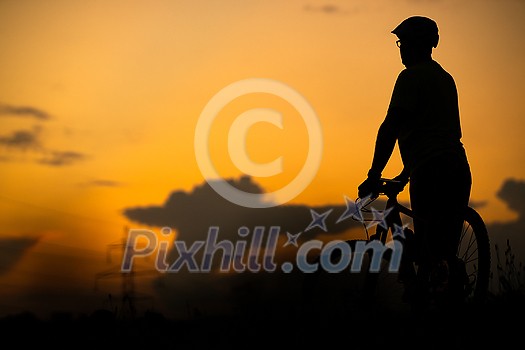Young man with his mountain bike going for a ride past the city limits in a lovely forest, getting the daily cardio dose - silhouette image against sunset sky