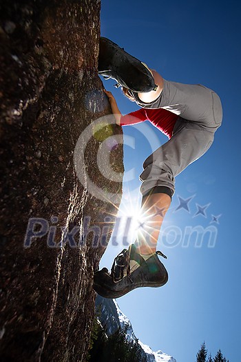 Young female climber putting climbing shoes on before climbing on a boulder outdoors, in Swiss Alps Young female climber putting climbing shoes on before climbing on a boulder outdoors, in Swiss Alps