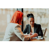 One-on-one meeting.Two young businesswomen sitting at a table in a cafe. Girl shows colleague information on the laptop screen. Girl using smartphone, blogging. Teamwork, business meeting. Freelancers working.