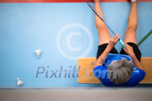 Badminton player resting after a tough match in a gym indoors - shot from above Badminton player resting after a tough match in a gym indoors - shot from above