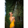 Beautiful young woman taking a shower outdoors. Attractive young woman in yellow one-piece enjoys shower on hot sunny day after a swim. Heat and refreshment concept.