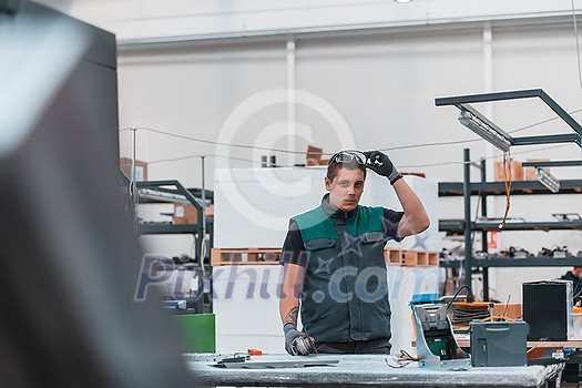 Heavy Industry Engineering Factory Interior with Industrial Worker Using Angle Grinder and Cutting a Metal Tube. Contractor in Safety Uniform and Hard Hat Manufacturing Metal Structures. High quality photo Heavy Industry Engineering Factory Interior with Industrial Worker Using Angle Grinder and Cutting a Metal Tube. Contractor in Safety Uniform and Hard Hat Manufacturing Metal Structures. High quality photo