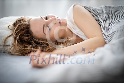 Pretty, young woman sleeping in her bed late in the morning on a weekend - compensating for the lack of sleep