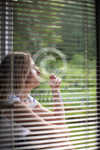 Mid-aged woman lighting a cigarette at home, getting her nicotine daily dose, unable to resist to her unhealthy habit Mid-aged woman lighting a cigarette at home, getting her nicotine daily dose, unable to resist to her unhealthy habit
