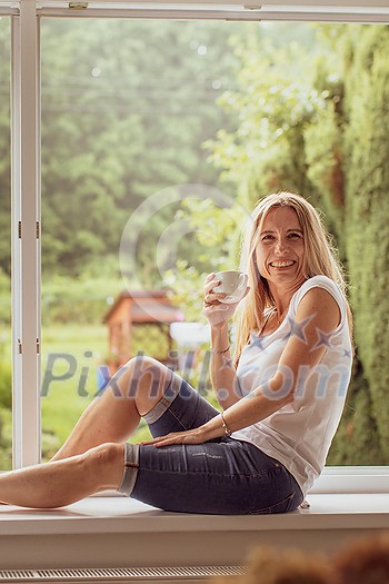 Mid-aged woman enjoying a cup of coffee in a window of her appartment