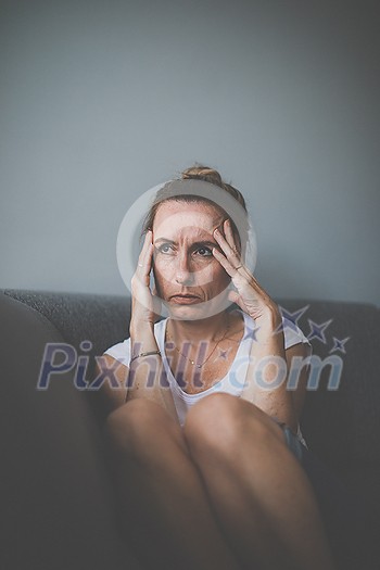 Depressed mid-aged woman at home feeling sad, lonely, anxious (color toned image)
