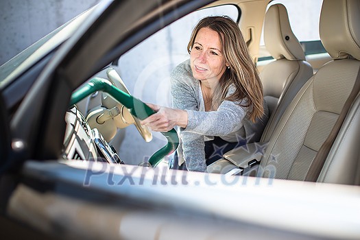 Pretty, middle aged woman vacuum cleaning the interior of a luxury car