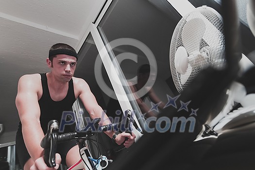 Man cycling on the machine trainer he is exercising in the home at night playing online bike racing game during coronavirus covid19 lockdown new normal Man cycling on the machine trainer he is exercising in the home at night playing online bike racing game during coronavirus covid19 lockdown new normal