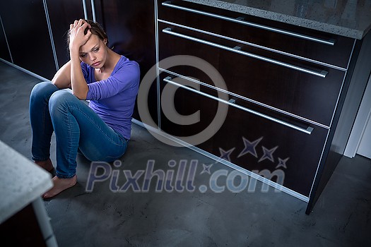 Depressed young woman, sitting on the kitchen floor, feeling down