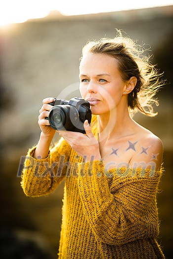 Hobby photographer concept. Outdoor lifestyle portrait of young woman taking photos with her mirrorless camera in warm evening sunlight