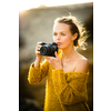 Hobby photographer concept. Outdoor lifestyle portrait of young woman taking photos with her mirrorless camera in warm evening sunlight