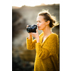 Hobby photographer concept. Outdoor lifestyle portrait of young woman taking photos with her mirrorless camera in warm evening sunlight