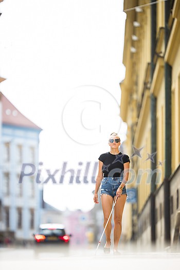 Blind woman walking on city streets, using her white cane to navigate the urban space better and to get to her destination safely Blind woman walking on city streets, using her white cane to navigate the urban space better and to get to her destination safely