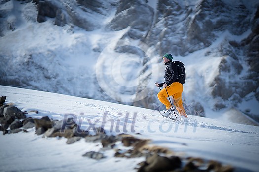 Winter sports - young man walking with snowshoes uphill in high mountains covered with lots of snow