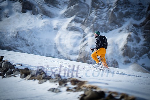 Winter sports - young man walking with snowshoes uphill in high mountains covered with lots of snow Winter sports - young man walking with snowshoes uphill in high mountains covered with lots of snow