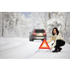 Pretty, young woman setting up a warning triangle and calling for assistance after her car broke down in the middle of nowhere on a freezing winter day