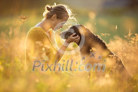 Pretty, young woman with her large black dog on a lovely sunlit meadow in warm evening light, playing together