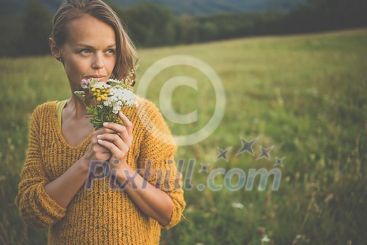 Beautiful young woman outdoors with a bouquet of wild flowers in a field, enjoying nature. Happy Woman on spring meadow