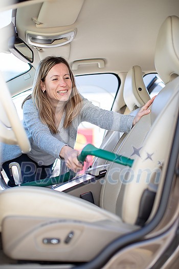Pretty, middle aged woman vacuum cleaning the interior of a luxury car