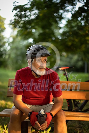 Senior man with his mountain bike going for a ride past the city limits in a lovely forest, getting the daily cardio dose, having a break on a bench
