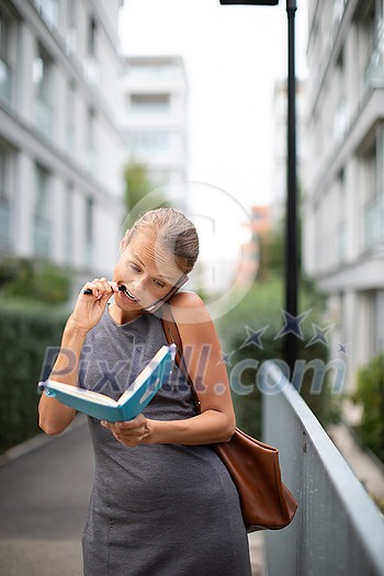 Busy personal assistant calling on the phone and taking notes at the same time while walking on the city street Busy personal assistant calling on the phone and taking notes at the same time while walking on the city street
