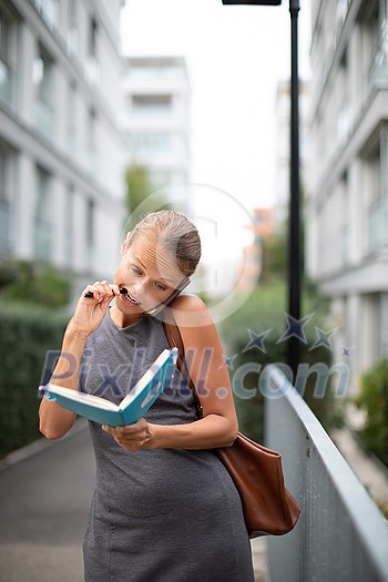 Busy personal assistant calling on the phone and taking notes at the same time while walking on the city street