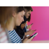 a group of diverse teenagers use mobile devices while posing for a studio photo in front of a pink background

