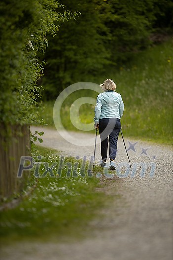 An elderly woman in nature Nordic walking outdoors. Healthy daily cardio routine.