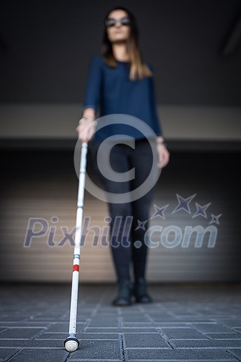 Blind woman walking on city streets, using her white cane to navigate the urban space better and to get to her destination safely Blind woman walking on city streets, using her white cane to navigate the urban space better and to get to her destination safely