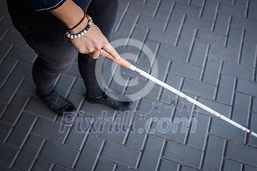 Blind woman walking on city streets, using her white cane to navigate the urban space better and to get to her destination safely Blind woman walking on city streets, using her white cane to navigate the urban space better and to get to her destination safely