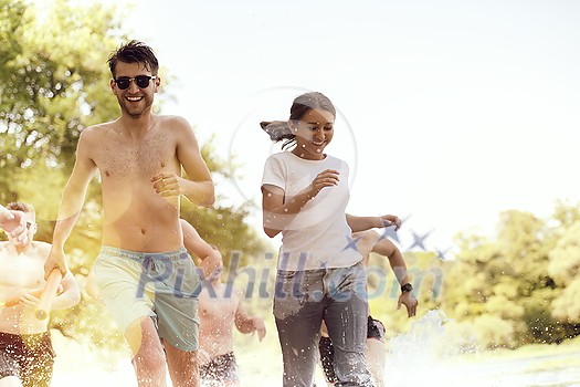 Summer joy group of happy friends having fun while running and splashing on river Summer joy group of happy friends having fun while running and splashing on river