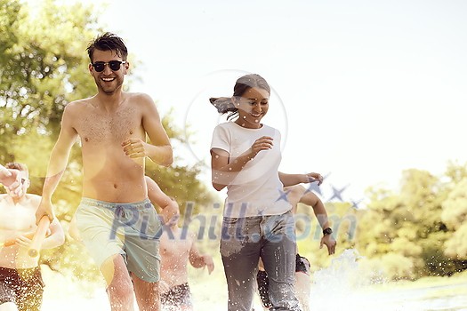 Summer joy group of happy friends having fun while running and splashing on river