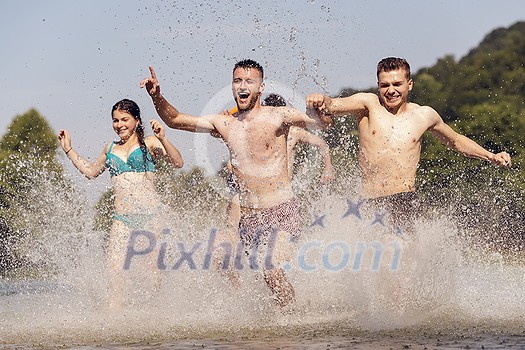 Summer joy group of happy friends having fun while running and splashing on river Summer joy group of happy friends having fun while running and splashing on river
