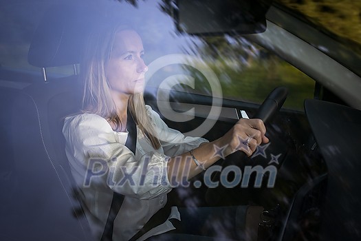 Pretty midle aged woman at the steering wheel of her car, going fast