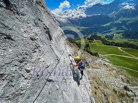 Pretty female climber on a steep Via Ferrata in the Swiss Alps - fearlessly climbing higher on this extreme alpine trail