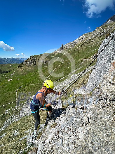 Pretty female climber on a steep Via Ferrata in the Swiss Alps - fearlessly climbing higher on this extreme alpine trail