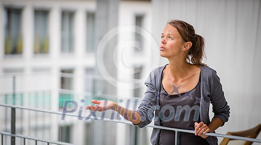 Is it going to rain? No, it is raining already. Young woman checking the weather from her balcony. Not happy about it.